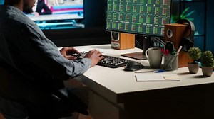 Financial advisor examines cryptocurrency trade market from his loft workstation, looks at online global exchange statistics on desktop. Guy studying stock analysis to secure capital funds. Camera B.