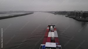 Container barge sailing on a dutch river near Rotterdam while a passenger ferry is navigating the other direction on the wrong side of the river on a misty day. Drone dolly slowmo shot.
