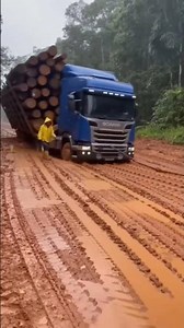 A truck loaded with logs nearly overturned on a rough, slippery, muddy road after the rain.