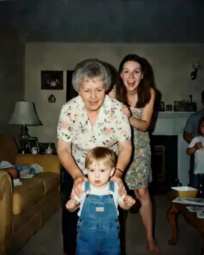 WE FOUND THIS OLD PHOTO TAPED INSIDE HER CLOSET—AND NOW NO ONE CAN AGREE WHO THE BABY IS It was folded once, taped behind her red coat. Not in a frame. Not labeled. Just left there. Same living room. Same lamp. Same smile on Aunt Shelby. But the kid in overalls? None of us recognize him. Grandma never mentioned another cousin. No birth announcements. No missing records in the albums she alphabetized every year since 1973. But there he is. Center of the frame. She’s holding him like he’s hers. We