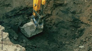 Big metallic excavator bucket scoops up ground . Ripper bucket excavating soil and rocks at a construction site . Close up bulldozer digging building foundation in slow motion. Tractor working