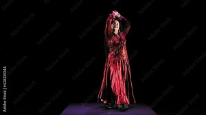 A barefoot gypsy woman with long hair in a red suit dances incendiaryly on a black background. Overall plan