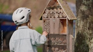 Little beautiful girl walking up to the insect hotel watching insects and bees outdoors