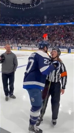 Female referee stops play and signals a major penalty lifting a red card toward a male player