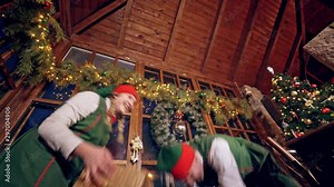 Two elves are standing in specially decorated room near the table and throwing presents to each other. Feast fireplace in the background. Christmas spirit concept close up video. Christmas eve. New Ye Stock Video