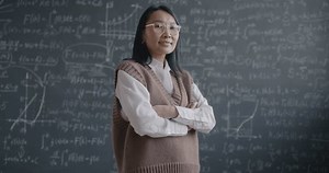 Slow motion portrait of Asian woman high school teacher standing in front of blackboard with mathematics formula smiling looking at camera. Education and science concept.