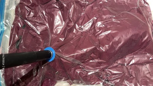 Vacuum storage process compressing winter jacket in plastic bag using vacuum pump. Home organization, space saving solution for clothing storage. Minimalist household and packing concept.