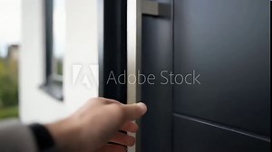 Man's hand reaching out to open the front door of a modern house.