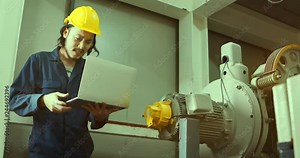Young Asian engineer using notebook near heavy machinery in industrial factory, he upset when he can't fix a problem, concept for engineer upset in industrial factory.