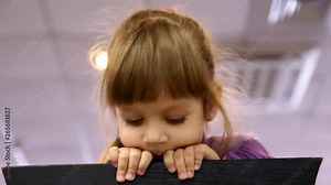 little girl looks out from behind a chair and hides