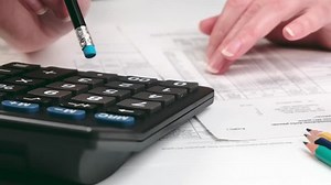 A hand holding a pencil makes calculations using a calculator. Close up of accountant or banker making calculations.
