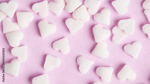 Sweet sugar sprinkles on pink background, macro video. Sprinkles of white sugars hearts, rotation. The concept of love and romance