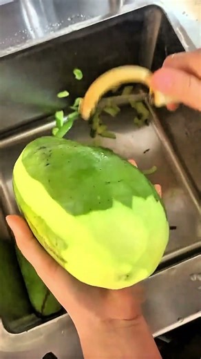 Peeling green mango skin with handheld peeler