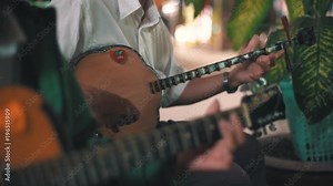 An elderly Vietnamese man plays the dan nguyet stringed instrument in a street performance with a guitar player in the foreground