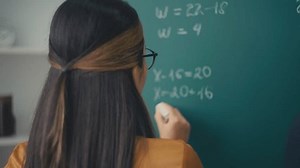 Female teacher writing math equations on board in school, education process, job
