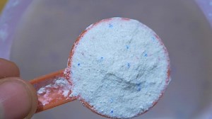Washing powder in plastic spoon on blue background