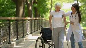 Doctor helping disabled old woman walking with crutches, recovery after trauma