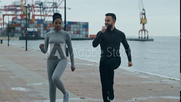 A fitness trainer guides a female client in knee lift exercises by the river, creating a dynamic outdoor training experience on a cloudy day