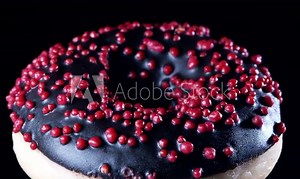 Donut rotates on a black background. The dark chocolate donut moves slowly. Donut with red powder.