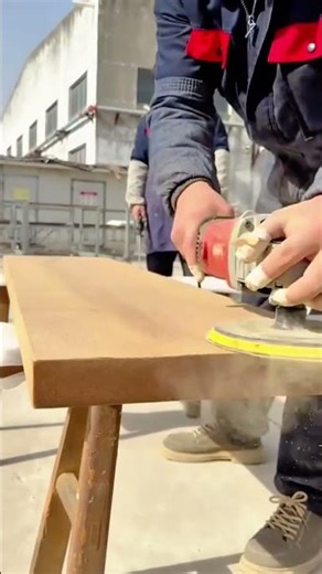 A worker using an orbital sander to smooth a wooden plank or tabletop