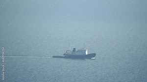 Tug boat in open calm sea, heading back to port at sunset, helps large container ships maneuver. Aerial view, maritime industry, oceanic transportation or business concepts.