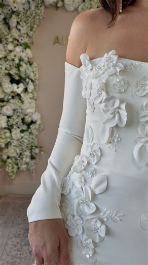 Meet A&V Exclusive gown, Margo! ✨ She’s the perfect blend of sculpted sophistication and soft romance — with 3-dimensional floral appliqués, hand-beaded pearls, and a flattering off-the-shoulder silhouette that feels both modern and timeless. Designed for the bride who loves texture, detail, and a touch of drama! | Aisle & Veil