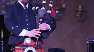 Bagpipe player in a kilt plays musical instrument at the stage