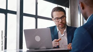 Two colleagues in suits talking at the desk
