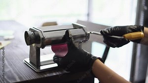 Master rolls polymer clay in pasta machine. Artisan works with plastic in workshop. Handmade concept.