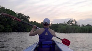 A woman is kayaking on a calm river. She is rowing with oars. 4K