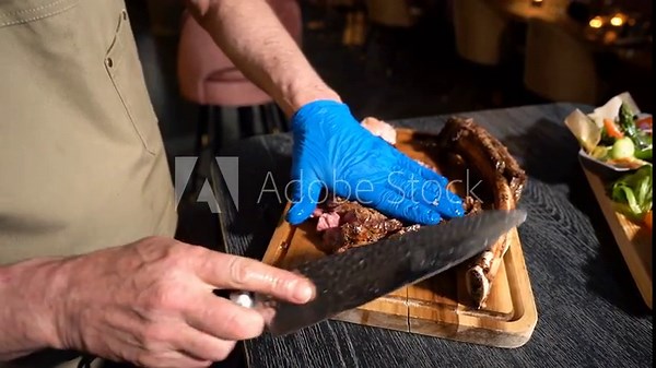 Process of cutting the steak with a large kitchen knife on a cutting board. Rack of beef meat is cut into pieces.
