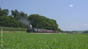 A 1924 Steam Engine with Passenger Train Puffing Smoke Traveling Along the Amish Countryside on a Summer Day