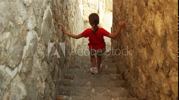 A girl navigates narrow, ancient stone stairs in old town of Stari Bar, Montenegro. She makes her way down, surrounded by rustic walls that tell a story of history. Ancient Mediterranean architecture