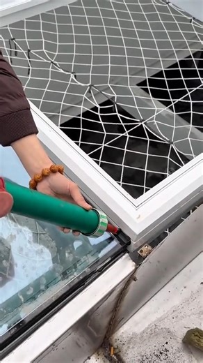 sealing a white window manually using a green metal tool for a very neat building finishing work
