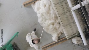 A factory worker stands at a flax processing machine and adjusts the flax with a long probe at the exit of the equipment. View from above