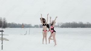 Girls frolic in the snow on the bank of a frozen river.