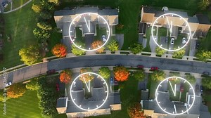 Suburban neighborhood street with overlayed clock graphics on rooftops. Autumn trees lining the road. Residential area with parked cars and green lawns. Aerial top down with animation. Passing time.