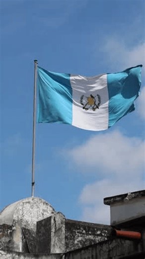 guatemala flag waving in the breeze above a historic colonial building in antigua (guatemalan blue and white flag with quetzal bird) blue sky latin america footage close up