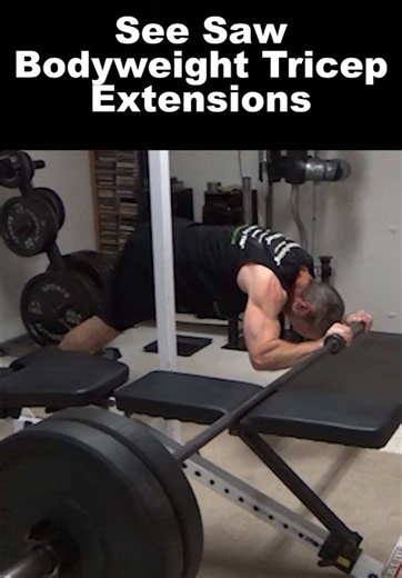 Your triceps (and six-pack abs) are going to HATE me for this one... IF you decide to try it...though probably even for just watching this video, to be honest. This is a See Saw Bodyweight Tricep Extension. I've got a barbell loaded with two 45 lb bumpers on one end to counterbalance, set across a flat bench (right in the center - no offset loading here). This creates the see saw setup. I weigh about 175 lbs to give you an idea of the weight to use for counterbalancing. I've got my hands set on 