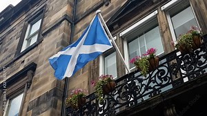 Camera moves past a Scottish flag waving in the breeze while hanging from a balcony flagpole, filmed in UHD 4K