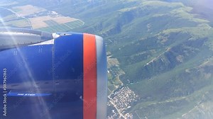 Airplane window view showing wing of the plane flying over land.
