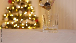 Pouring Whiskey from a bottle into a Glass during xmas holiday with a blurred decorated Christmas tree in the background