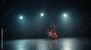 Silhouette of young ballet dancer in pointe shoes and flowing dress. Graceful ballerina dancing elements of classical ballet on stage in backlight of spotlights