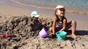 Children girls playing with sand at the beach in summer day. Kids building sand sculptures with shovels and buckets on coast sea. Fun family vacation concept