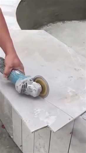 cutting large grey floor tiles precisely using an electric hand grinder tool at a construction site