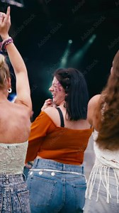 Vertical video rear view of three female friends having fun dancing at outdoor summer music festival - shot in slow motion