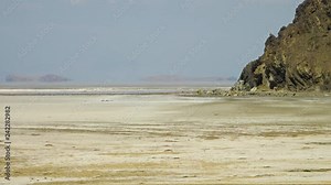 Dash-e Kavir Desert, Iran, with a heat haze over the flat, salty plains. Rocky mountains in the background covered in low-lying shrubs.