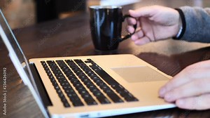 Clip taken at coffee shop cafe of a caucasian man typing on computer keyboard then drinking from a coffee cup. Shot in 4k 60fps and slowed down to 50% on a 30fps timeline. Stock Video