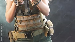 Portrait of a beautiful woman warrior in military outfit with firearm in hands, aiming at enemy, fighting in smoke from exploding shells at night. Slow motion