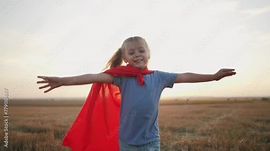 girl with the cloak. concept of a happy childhood and family for a child. a little girl in a superhero costume runs across a lifestyle field, a red cape and a blue T-shirt, sunset on the background